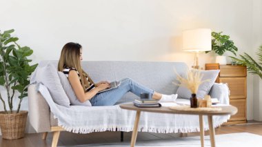 Woman using laptop to work or do homework at home with smiling face in her living room, Creating happiness at work with a smile, Live performance or video call with laptop, Work from home.