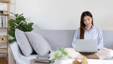 Woman using laptop to work or do homework at home with smiling face in her living room, Creating happiness at work with a smile, Live performance or video call with laptop, Work from home.