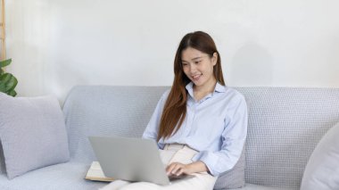 Woman using laptop to work or do homework at home with smiling face in her living room, Creating happiness at work with a smile, Live performance or video call with laptop, Work from home.