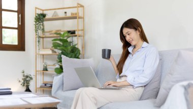 Woman using laptop to work or do homework at home with smiling face in her living room, Creating happiness at work with a smile, Live performance or video call with laptop, Work from home.