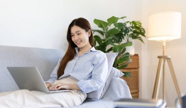 Woman using laptop to work or do homework at home with smiling face in her living room, Creating happiness at work with a smile, Live performance or video call with laptop, Work from home.