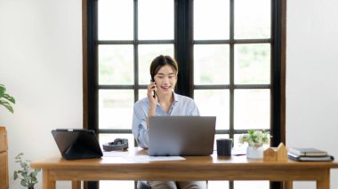 Woman working at home, Attractive woman chatting or talking with colleague on mobile phone at her home, Work for home, Remote conversation or meeting , Stay home, Use a cell phone or smartphone.