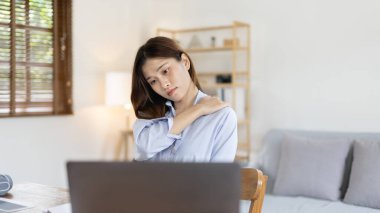 Asian woman sore muscles and neck after sitting at work or homework for a long time, Suffering from muscle aches and tendon pressure, Massage your shoulders to relax your muscles, Work from home.