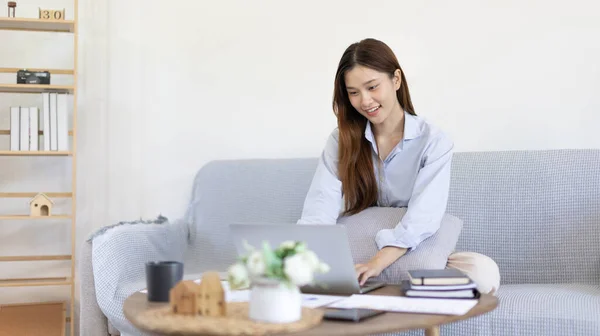 Woman using laptop to work or do homework at home with smiling face in her living room, Creating happiness at work with a smile, Live performance or video call with laptop, Work from home.
