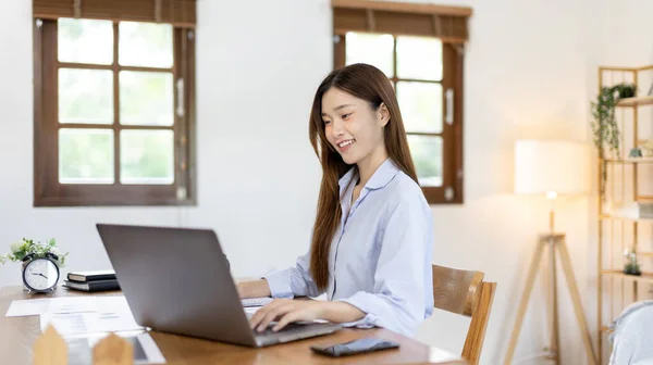 Woman using laptop to work or do homework at home with smiling face in her office, Creating happiness at work with a smile, Live performance or vdo call with laptop, Work from home.