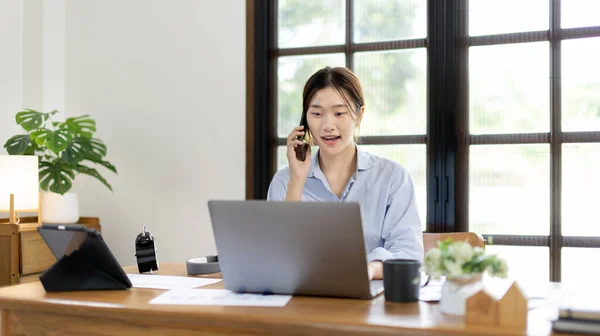 Woman working at home, Attractive woman chatting or talking with colleague on mobile phone at her home, Work for home, Remote conversation or meeting , Stay home, Use a cell phone or smartphone.