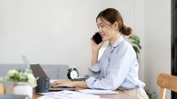Woman working at home, Attractive woman chatting or talking with colleague on mobile phone at her home, Work for home, Remote conversation or meeting , Stay home, Use a cell phone or smartphone.