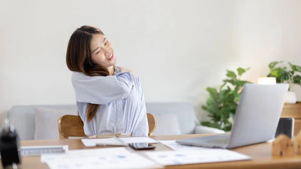 Asian woman sore muscles and neck after sitting at work or homework for a long time, Suffering from muscle aches and tendon pressure, Massage your shoulders to relax your muscles, Work from home.