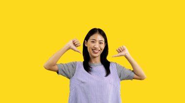 Young Asian woman pointing finger at herself, Concept of love yourself and believe in yourself, self esteem, Pointing two thumbs at herself, Isolated over yellow background.