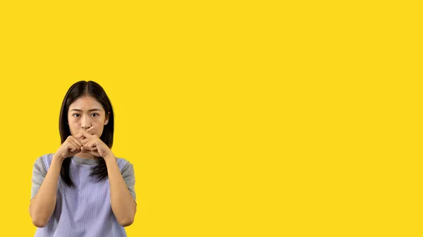 Asian woman doing silent gesture with finger, Noiseless signal transmission, Noiseless symbol, Hide a secret, Crossed hands, Do not speak, Shut your mouth, Isolated on yellow background .