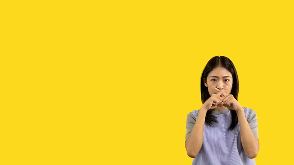 Asian woman doing silent gesture with finger, Noiseless signal transmission, Noiseless symbol, Hide a secret, Crossed hands, Do not speak, Shut your mouth, Isolated on yellow background .