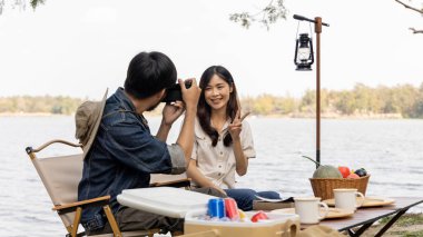 Camping for the weekend in the woods near the river, Relaxation activities for young couples, Woman using mobile phone to take a selfie with her boyfriend, Young couple outdoor leisure activities.