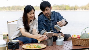 Young couple camping weekend in the woods near river, Enjoying Camping Holiday In Countryside, Leisure activities, Dating and relaxation in nature, Couple dripping coffee and sipping coffee.