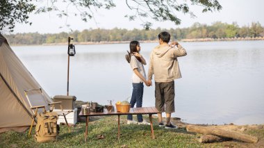 Couple camping for the weekend in the woods near the river, Camping Holiday In Countryside, Camping for the day and recreational activities amidst nature and relaxation, Outdoor leisure activities.