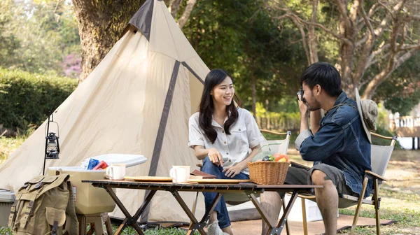 Camping for the weekend in the woods near the river, Relaxation activities for young couples, Woman using mobile phone to take a selfie with her boyfriend, Young couple outdoor leisure activities.
