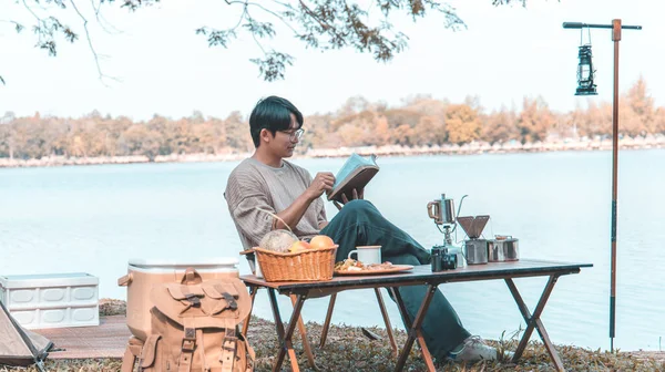 Young man camping for the weekend in the woods near the river, Camping Holiday In Countryside, Man sitting and relaxing happily reading definitions, Young man outdoor leisure activities.