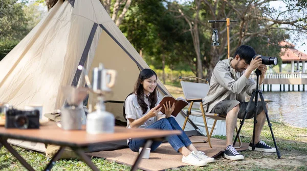 Young couple camping for the weekend in the woods near the river, Enjoying Camping Holiday In Countryside, Spend the holidays relaxing with novels and photography in nature, Young outdoor leisure activities.