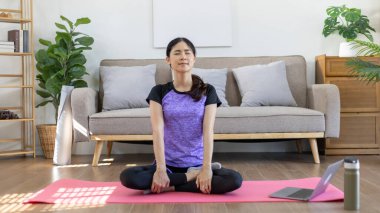 Beautiful healthy woman practicing yoga, Stretch or warm up before exercising, Calming the mind and meditating in her living room, Dumbbells and a protein shake or bottle of water, Healthy exercise.