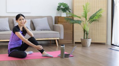 Beautiful healthy woman practicing yoga, Stretch or warm up before exercising, Calming the mind and meditating in her living room, Dumbbells and a protein shake or bottle of water, Healthy exercise.