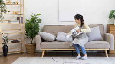 Pretty woman vacuuming the pillows and sofa in her living room, Big cleaning in the house, Removes germs, Housewife cleaning, Keeping her home clean, Domestic hygiene.