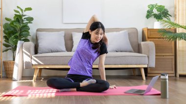 Beautiful healthy woman practicing yoga, Stretch or warm up before exercising, Calming the mind and meditating in her living room, Dumbbells and a protein shake or bottle of water, Healthy exercise.