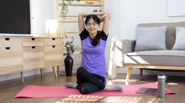 Beautiful healthy woman practicing yoga, Stretch or warm up before exercising, Calming the mind and meditating in her living room, Dumbbells and a protein shake or bottle of water, Healthy exercise.