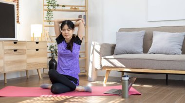 Beautiful healthy woman practicing yoga, Stretch or warm up before exercising, Calming the mind and meditating in her living room, Dumbbells and a protein shake or bottle of water, Healthy exercise.