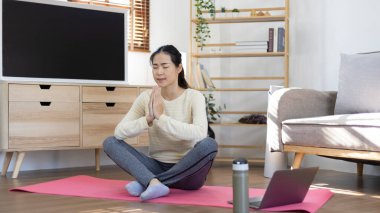 Beautiful healthy woman practicing yoga, Stretch or warm up before exercising, Calming the mind and meditating in her living room, Dumbbells and a protein shake or bottle of water, Healthy exercise.