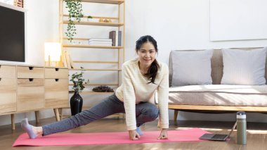 Beautiful healthy woman practicing yoga, Stretch or warm up before exercising, Calming the mind and meditating in her living room, Dumbbells and a protein shake or bottle of water, Healthy exercise.