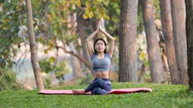 Ormanda yoga yapan Asyalı kadın, meditasyon ve nefes egzersizleri, dikkat eksikliğini tedavi edin ve zihninizi sakin, sağlıklı egzersiz, farkındalık, Homeopati, Park yogası için eğitin..