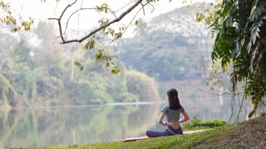 Ormanda yoga yapan Asyalı kadın, meditasyon ve nefes egzersizleri, dikkat eksikliğini tedavi edin ve zihninizi sakin, sağlıklı egzersiz, farkındalık, Homeopati, Park yogası için eğitin..