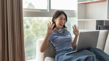 Genç Asyalı kadın, arkadaşları ve öğretmenlerini yüzünde gülümseme, internet iletişimi, evde kalmak, yeni normal, VDO çağrısı, sosyal mesafe, internet öğrenimi ile canlı bir videoda selamlıyor..