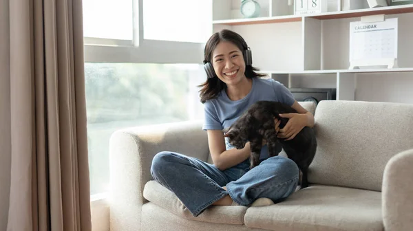 Young woman relaxing on sofa with her adorable black American Shorthair cat happily, Owner\'s favorite pet, Love relationship between people and pets, Woman sitting on the sofa in living room.