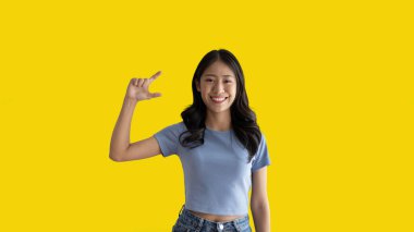 Asian woman with holding copyspace imaginary on the palm to insert an ad, Showing copyspace pointing, Showing her hand to present something on yellow background.