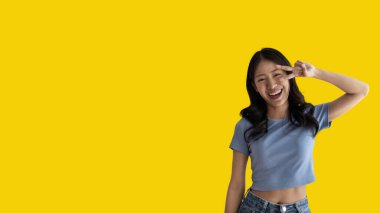 Young Asian woman making two thumbs up gesture showing joy and fun, Symbol of good friendship, Popular photo poses, Make a v-shaped finger, Yellow background.