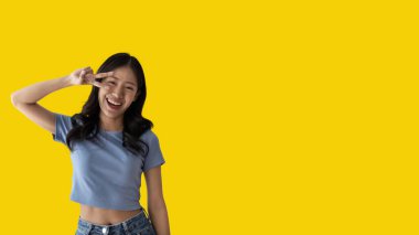 Young Asian woman making two thumbs up gesture showing joy and fun, Symbol of good friendship, Popular photo poses, Make a v-shaped finger, Yellow background.