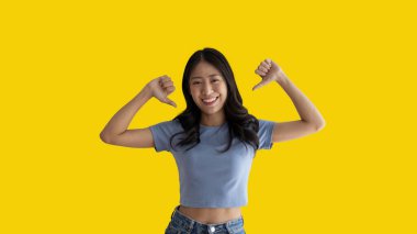 Young Asian woman pointing finger at herself, Concept of love yourself and believe in yourself, self esteem, Pointing two thumbs at herself, Isolated over yellow background.