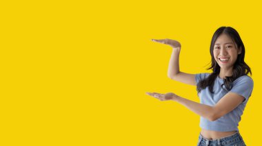 Asian woman with holding copyspace imaginary on the palm to insert an ad, Showing copyspace pointing, Showing her hand to present something on yellow background.