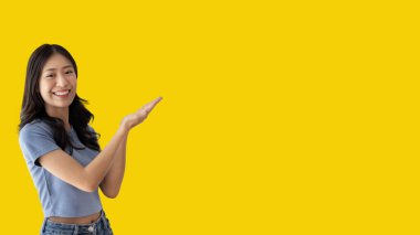 Asian woman with holding copyspace imaginary on the palm to insert an ad, Showing copyspace pointing, Showing her hand to present something on yellow background.