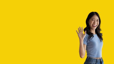 Waving hand in hi, Asian woman smiling friendly greeting, Hello,nice to meet you,say hi, Say hi and greet you, Welcome new people Join a multicultural team, Goodbye, Isolated on yellow background.