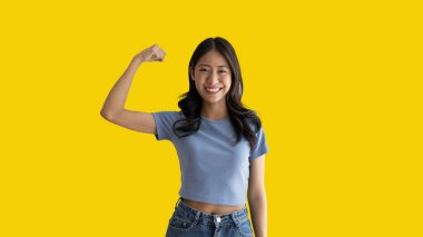 Woman flexing her muscles, Young Asian woman shows off her strength by flexing her jaw and showing off her power, Healthy, Happiness of your choice, Yellow background.