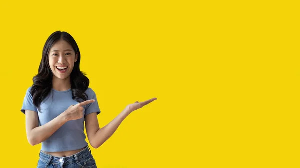 stock image Asian woman with holding copyspace imaginary on the palm to insert an ad, Showing copyspace pointing, Showing her hand to present something on yellow background.
