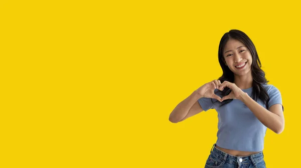 Asian young woman with bright smile making heart symbol shape with hands, Symbol of love and romance, Give each other cuteness and create smiles for each other, Positive thinking concept.