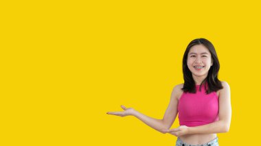 Asian woman with holding copyspace imaginary on the palm to insert an ad, Showing copyspace pointing, Showing her hand to present something on yellow background.