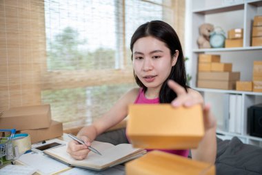 Kadın, bilgilere göre nakliyeye hazırlanmak için müşteri bilgilerini ve adreslerini not defterine ya da posta kutusuna yazıyor. Paketleme kutusu, çevrimiçi satış, serbest çalışma..