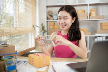 Kadın kimlik doğrulama ya da sipariş onayı için cep telefonuyla ürün ve posta kutusunun fotoğrafını çekiyor, iş stili evde çalışıyor, evde çalışıyor ve işletme sahibi oluyor..