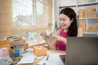 Kadın kimlik doğrulama ya da sipariş onayı için cep telefonuyla ürün ve posta kutusunun fotoğrafını çekiyor, iş stili evde çalışıyor, evde çalışıyor ve işletme sahibi oluyor..