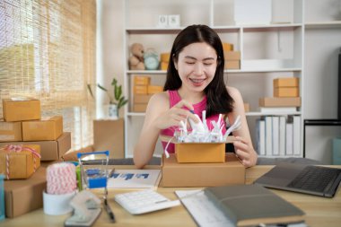 Bir müşteriye teslimat için hazırlanmak üzere eşyaları posta kutusuna koyan kadın, evde çalışıyor ve işletme sahibi, çevrimiçi alışveriş yapan KOBİ girişimcisi, paket kutusu, çevrimiçi satış, serbest çalışma.