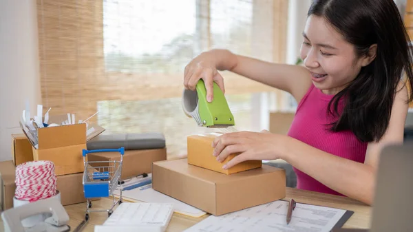 Woman packing items into a post box to prepare for delivery to a customer, Working at home and owning businesses, Online shopping SME entrepreneur, packing box, Sell online, freelance working.