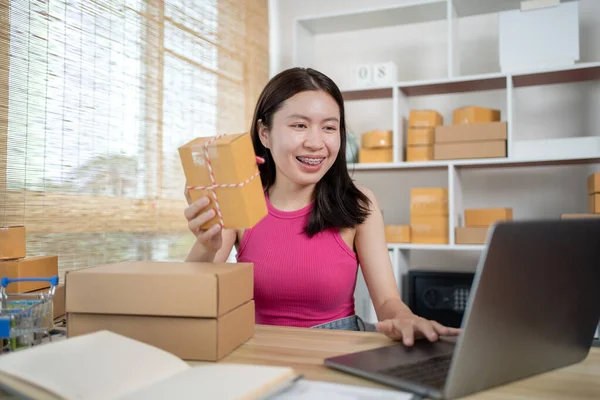 Woman uses a laptop to chat with customers who come to order product, Freelance work at home, Packaging on background, Sell online, Small business owner, Online shopping SME entrepreneur.